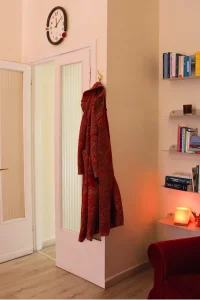 Dettaglio dell&rsquo;ingresso dello studio di psicologia Cinque Vie con cappotto appeso e libreria illuminata, ambiente accogliente e rilassante